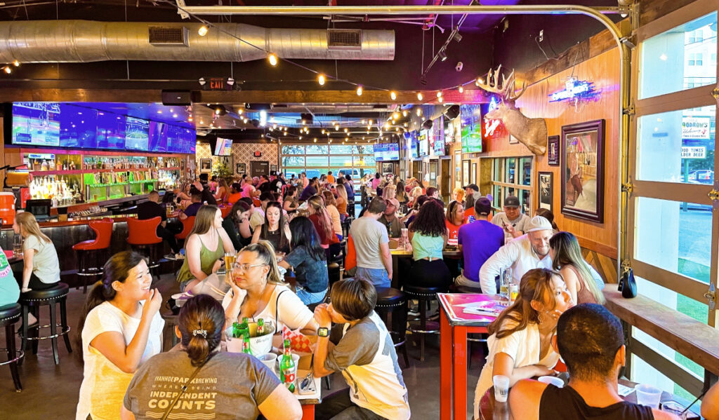 An indoor sports bar with crowds talking and watching TVs