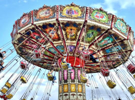 A carnival ride spins as people in bucket seats are hoisted into the air