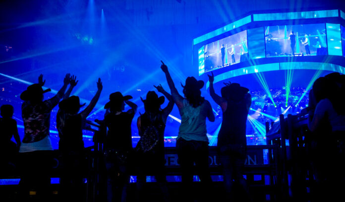 Women in cowboy hats silhouetted against a blue-lit arena