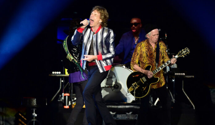 Mick Jagger singing on stage while Keith Richards plays guitar behind him