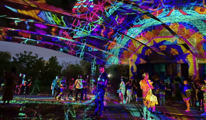 People standing under a bridge covered in a projection of colors and shapes