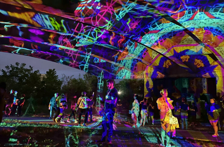 People standing under a bridge covered in a projection of colors and shapes