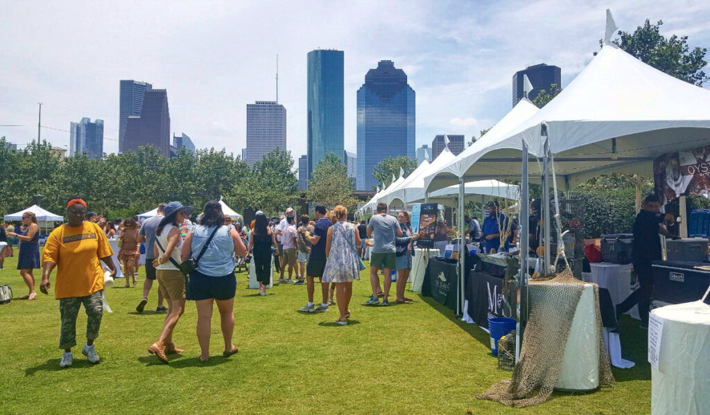 An outdoor festival of people strolling by stalls with the Downtown skyline in the background