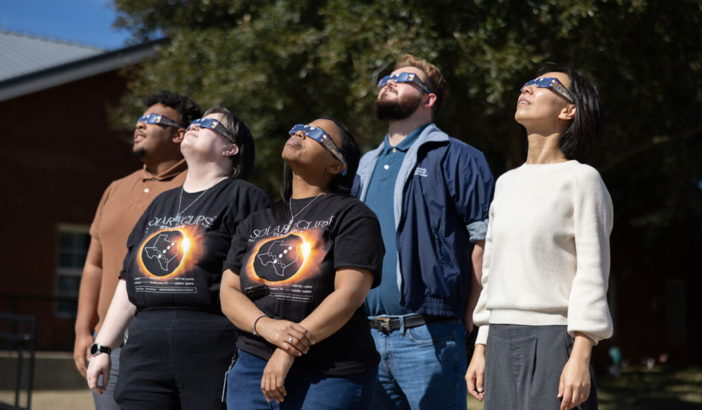 Five people wearing eclipse viewing glasses looking to the sky