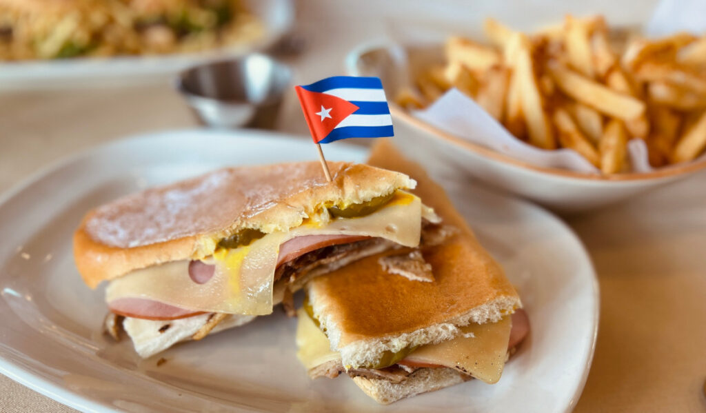 Two halves of a sandwich on a plate with a Cuban flag toothpick