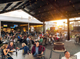 A covered outdoor patio with people sat at tables and the sun setting