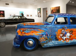A blue car with painted flames and intricate artwork in a gallery space