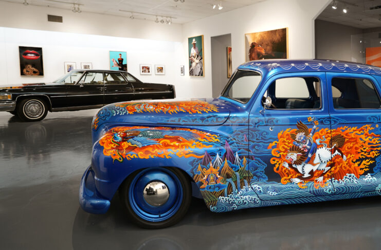 A blue car with painted flames and intricate artwork in a gallery space