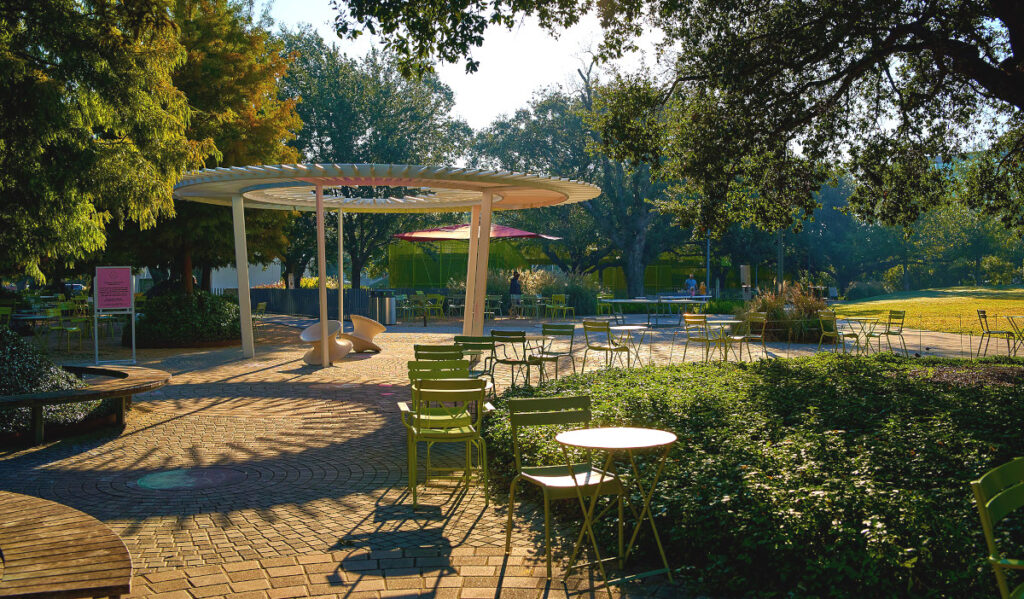 A row of tables and chairs rounds a brick pathway with an overhead structure