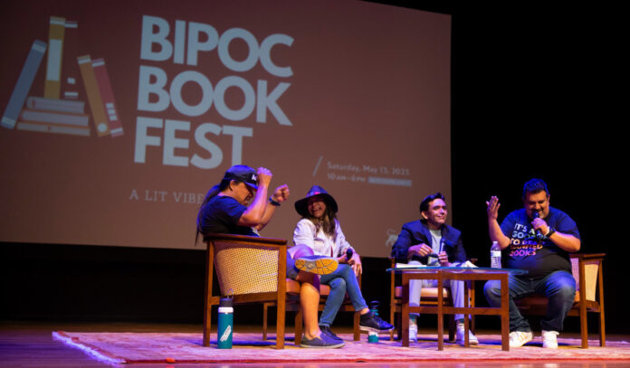 Four panelists on a stage in discussion with a projection of "BIPOC Book Fest" behind them