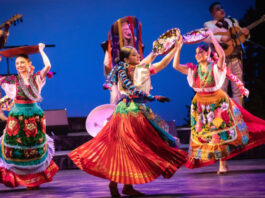 Three ballet folklorico dancers holding ceramics above their head and twirling