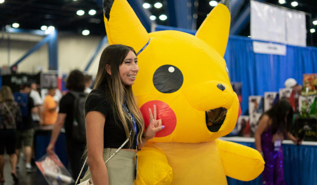 A girl posing next to a cosplayer in Pikachu costume, holding up the peace sign