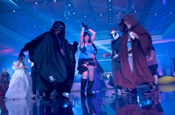 Fans cosplaying as Lara Croft and Star Wars characters dance in a blue-lit room