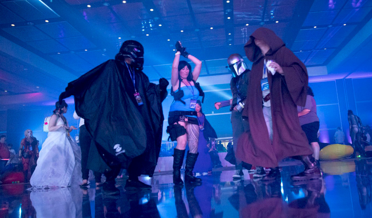Fans cosplaying as Lara Croft and Star Wars characters dance in a blue-lit room