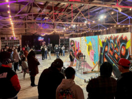 Artists paint graffiti on walls surrounded by a crowd of people