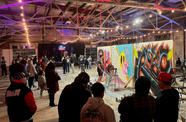 Artists paint graffiti on walls surrounded by a crowd of people