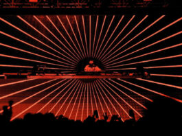 A DJ on stage in front of screens with red radial lines