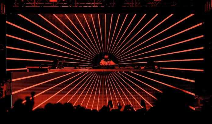 A DJ on stage in front of screens with red radial lines