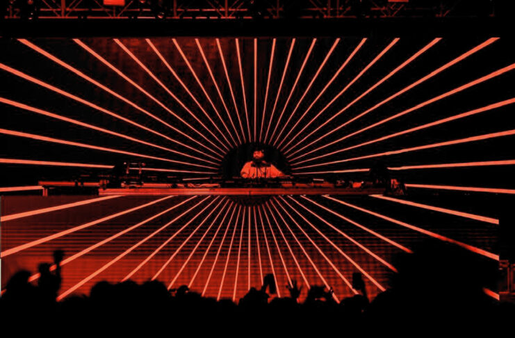 A DJ on stage in front of screens with red radial lines