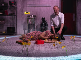 A man kneels over a sleeping character next to a box of chocolates and small yellow flowers
