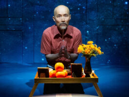 A man kneeling before a table with flowers, oranges and photos