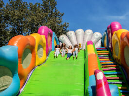 Four girls sliding down a bright green inflatable slide on a sunny day