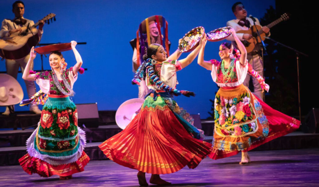 Three ballet folklorico dancers holding ceramics above their head and twirling