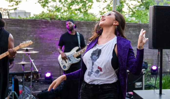 A woman in a purple coat and Prince t-shirt dances to a band