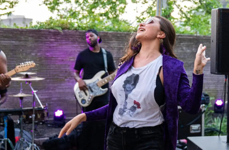 A woman in a purple coat and Prince t-shirt dances to a band