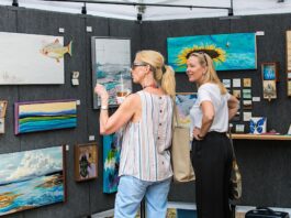 Two women looking at a wall of artwork and discussing