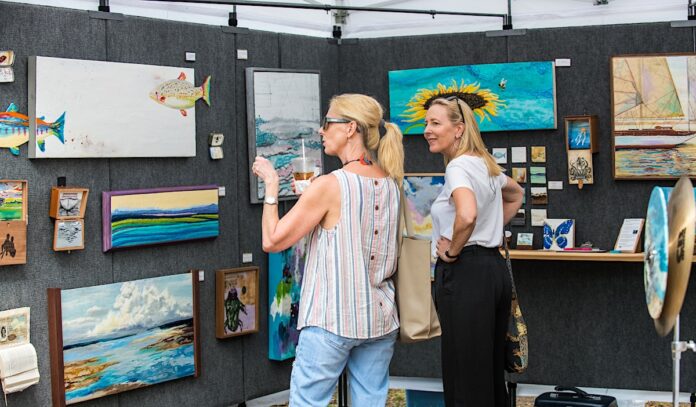 Two women looking at a wall of artwork and discussing