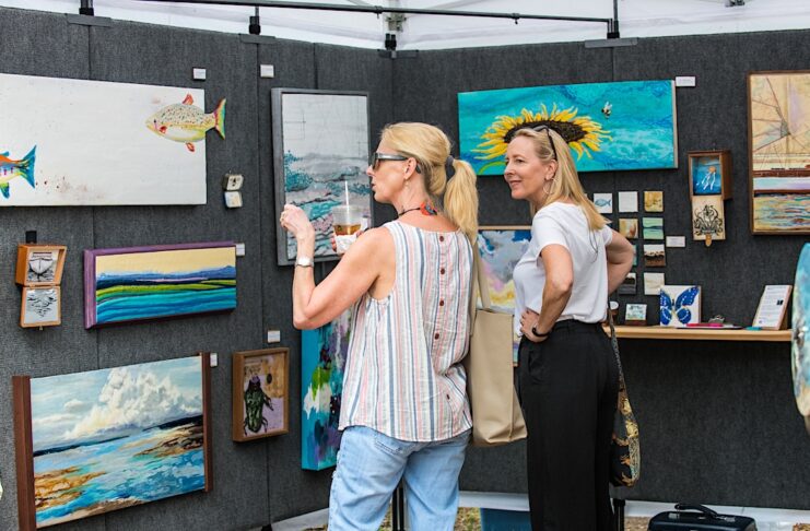 Two women looking at a wall of artwork and discussing