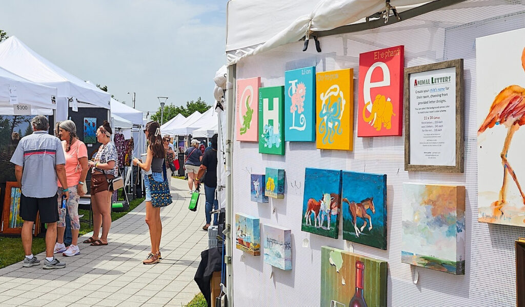 An art stall with framed paintings next to a walkway with several people standing on it