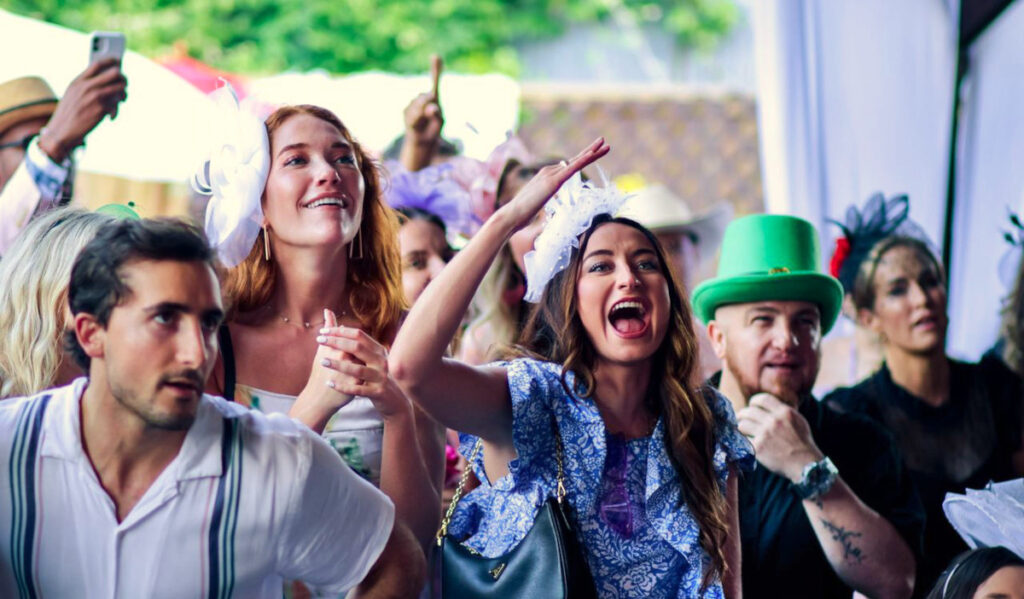 A crowd of people reacting with excitement to a horse race out of camera view