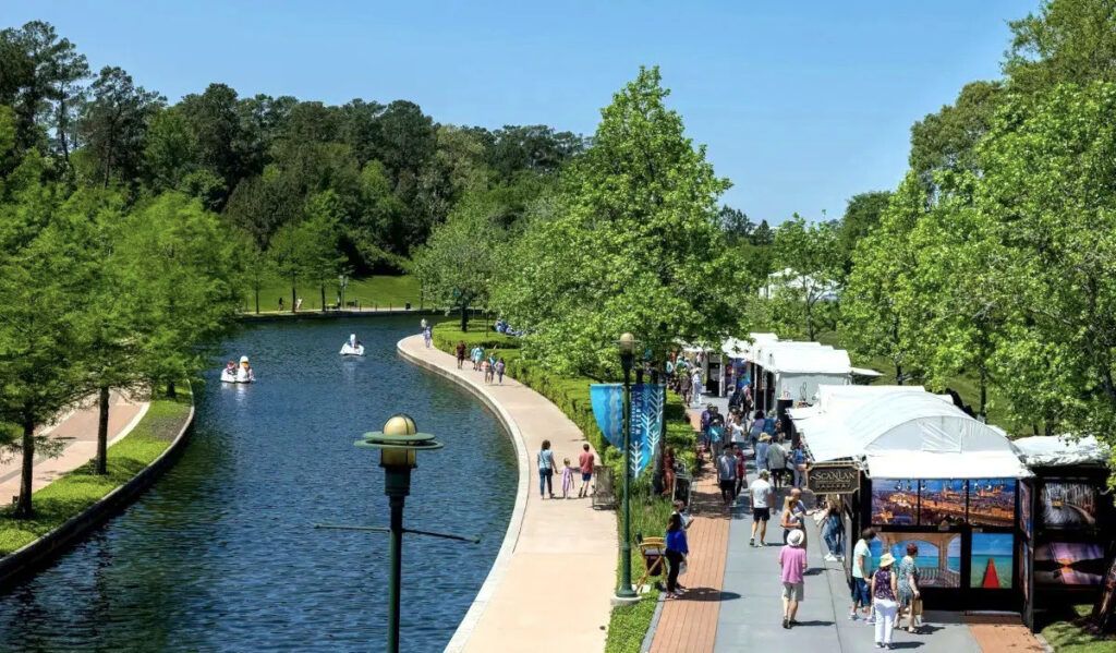 People strolling by vendor booths on the shore of a waterway, with people pedaling swan boats