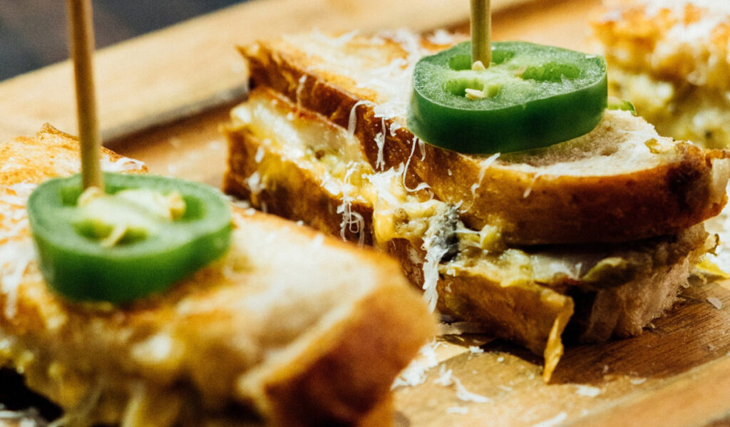 A close up of sandwich halves, topped with a slice of jalapeno and shredded cheese