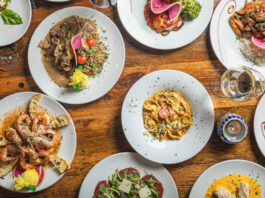 An overhead view of ten dishes, including pasta, shrimp, and carpaccio