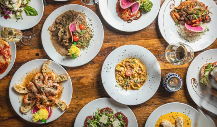 An overhead view of ten dishes, including pasta, shrimp, and carpaccio