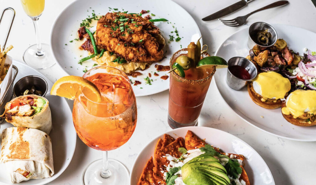 A brunch spread with Bloody Mary and other drinks, and four plates of food topped with garnishes and sauced