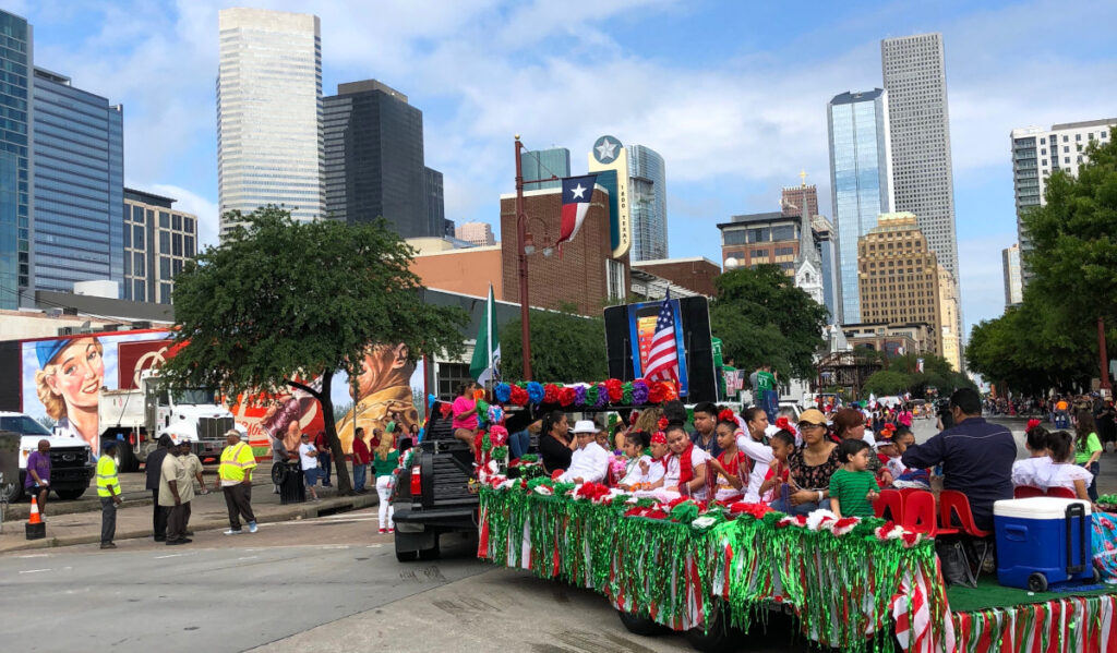 A parade float turning a corner with the downtown Houston skyline in the background