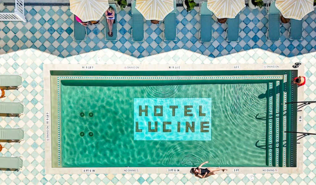 An overhead aerial of a pool with the words "Hotel Lucine" at the bottom, and three women relaxing around it