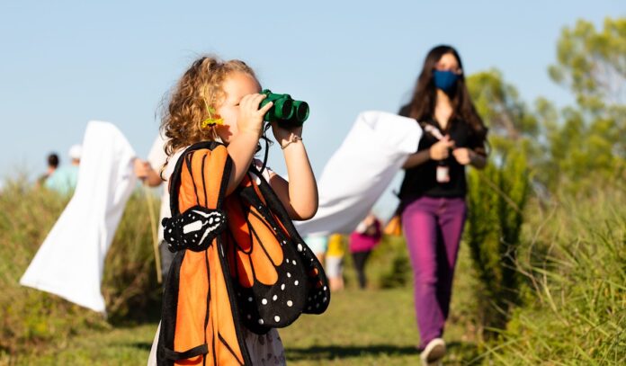 A child looking through binoculars while wearing butterfly clothing