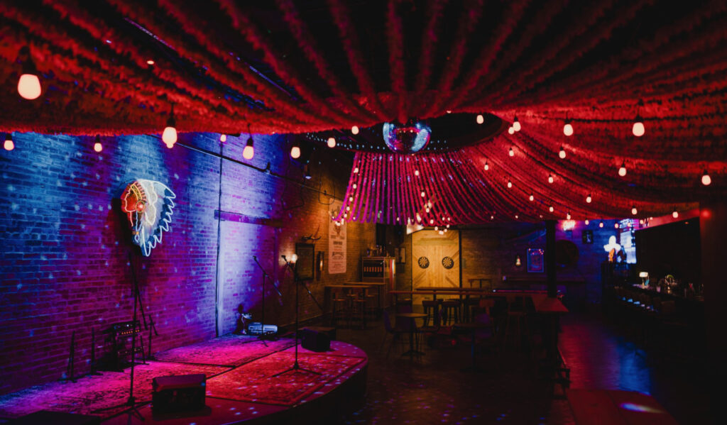 An empty bar with a stage, dart boards and strands of garland hanging from the ceiling