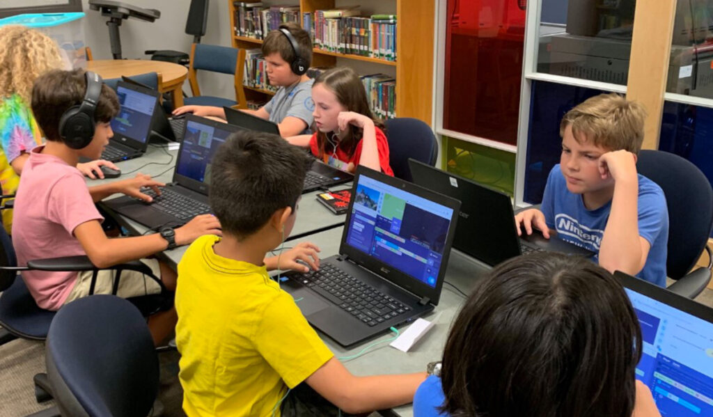 Eight children sitting at a table looking at laptop screens