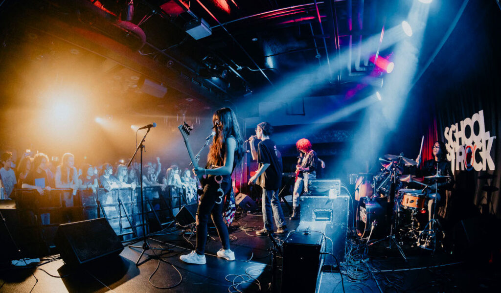 A rock band of children musicians performs to a crowd