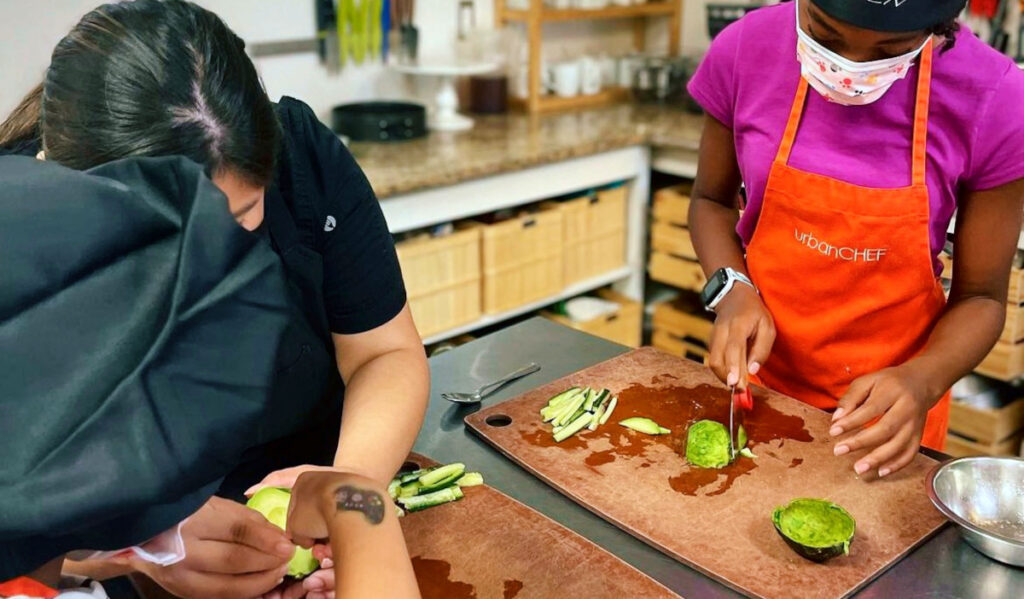 Three kids standing around cutting boards slicing an avocado