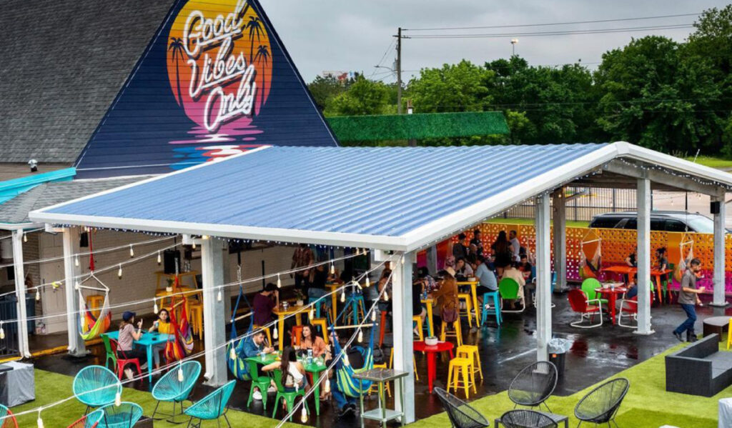 An aerial view of a building that says "Good Vibes Only" with a colorful covered patio with people