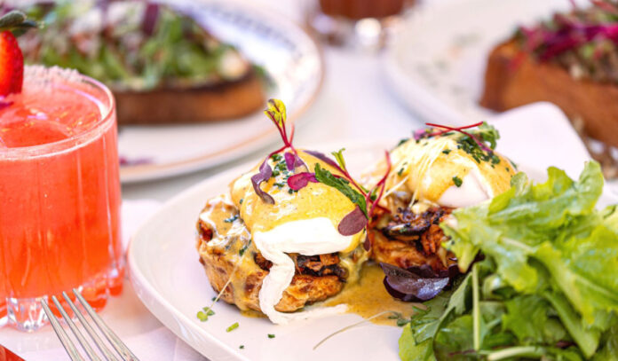 A close up of eggs benedict next to a pink cocktail