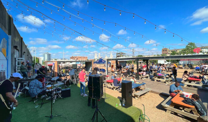 A band plays on an outdoor stage while picnic tables full of people surround