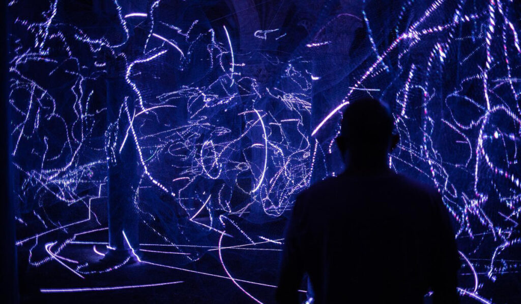 A silhouetted figure stands in front of a tangle of lights in an installation